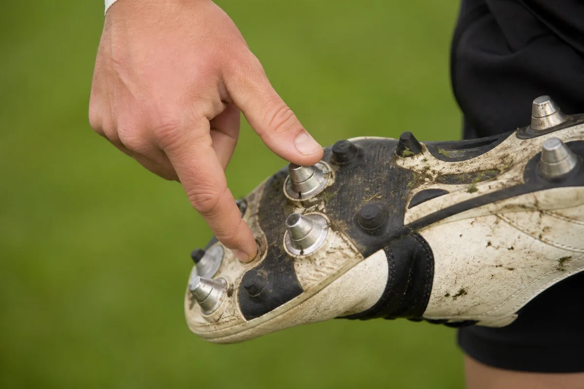 Contrôle des crampons avant un match, main d&rsquo;arbitre inspectant la semelle d&rsquo;une chaussure de rugby