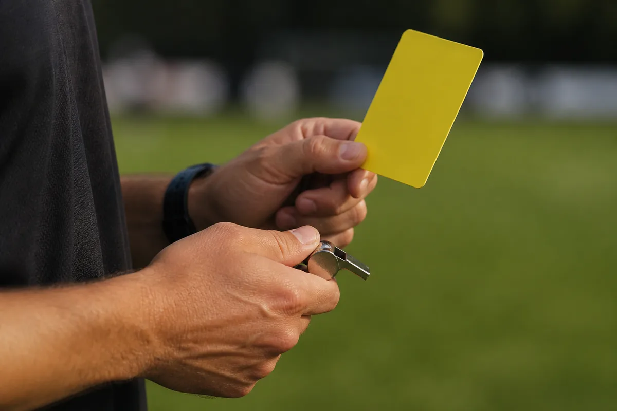 Arbitre de rugby en tenue sombre au centre d&rsquo;un terrain, sifflet à la main, lumière rasante de fin d&rsquo;après-midi