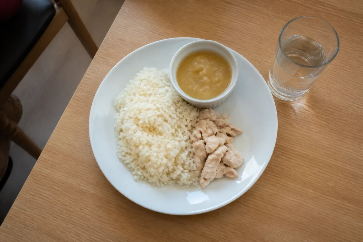 Assiette de riz blanc, de blanc de volaille et de compote posée sur une table en bois dans un club sportif